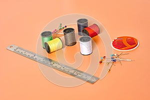 Scattered needles, metal ruler and spools with colorful threads on orange tailors desk in workshop