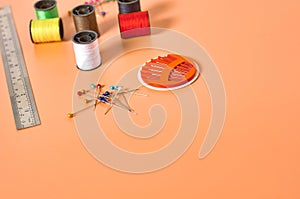 Scattered needles, metal ruler and spools with colorful threads on orange tailors desk in workshop