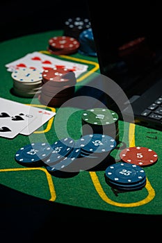 Scattered poker chips and cards on a green table with and laptop