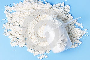 Scattered protein and measuring spoon on blue background top view, concert of sports nutrition