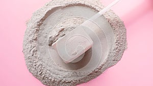 Scattered protein and measuring spoon on pink background, concept of sports nutrition.