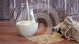 Scattered quinoa grains and a jug of milk on a wooden table. Chenopodium quinoa. milk from quinoa. flexitarian drink, protein shak