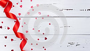 Scattered red hearts, satin ribbon on a white wooden background. Valentine`s day. Top view, free space for text, flatly