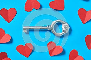 Scattered red paper hearts near silver vintage key lies on blue countertop. Concept of closed or opened love or Valentines day