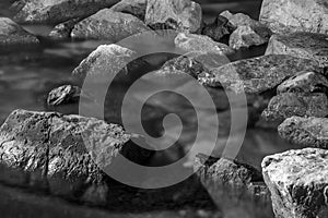 Scattered rocks and stones with visible texture immersed in sea water. Monochromatic, black and white composition.