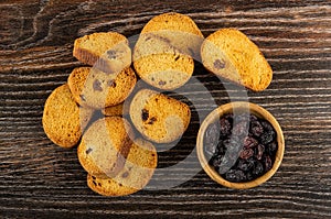 Scattered rusks with raisin, dried grape in bowl on wooden table. Top view