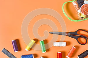 Scattered sewing accessories handbag, metal ruler, scissors and spools with colorful threads on orange tailors desk in workshop