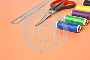 Scattered sewing accessories metal ruler, scissors and spools with colorful threads on orange tailors desk in workshop