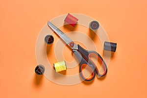 Scattered sewing accessories scissors and spools with colorful threads on orange tailors desk in workshop