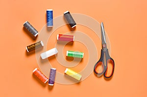 Scattered sewing accessories scissors and spools with colorful threads on orange tailors desk in workshop