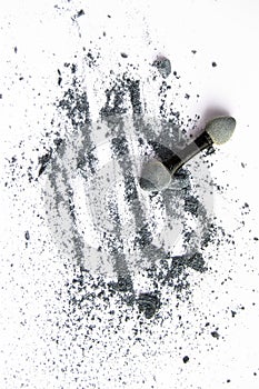 Scattered shiny powder blast, gray eyeshadow and makeup brush isolated on white background, vertical shot