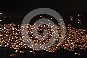 Scattered shiny roasted coffee beans on a black background with copy space
