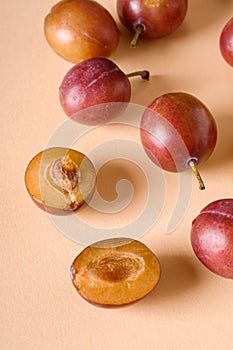 Scattered sliced half ripe sweet plum fruits with water drops on cream colored background