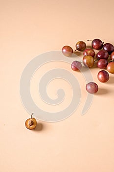 Scattered sliced half ripe sweet plum fruits with water drops on cream colored background, bright, angle view, copy space