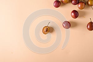 Scattered sliced half ripe sweet plum fruits with water drops on cream colored background, bright, top view, flat lay, copy space