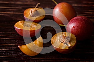 Scattered sliced half ripe sweet plum fruits with water drops on dark moody wood table background