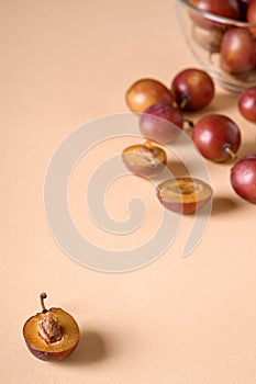 Scattered sliced half ripe sweet plum fruits with water drops near to plums in glass bowl on cream colored background