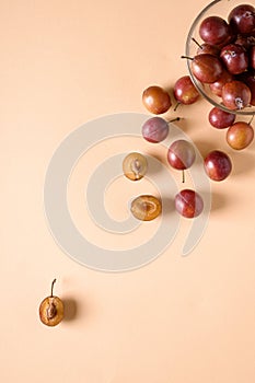 Scattered sliced half ripe sweet plum fruits with water drops near to plums in glass bowl on cream colored background