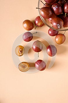 Scattered sliced half ripe sweet plum fruits with water drops near to plums in glass bowl on cream colored background