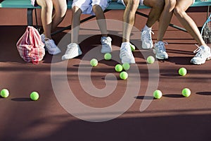 Scattered Tennis Balls On Court By Feet Of People photo