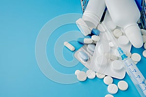 Scattered variety pills, drugs, spay, bottles, thermometer, syringe and empty shopping trolley cart on blue background. pharmacy