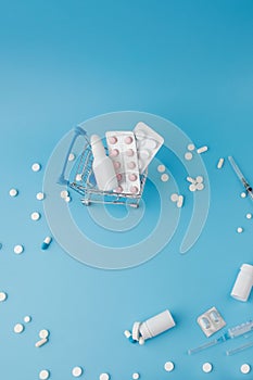 Scattered variety pills, drugs, spay, bottles, thermometer, syringe and empty shopping trolley cart on blue background. pharmacy