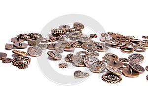 Scattered vintage steampunk copper metal buttons on a white background, shaped as gears, hearts, and clock pieces