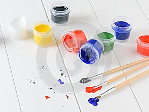 Scattered on a wooden table jars of gouache and three multi-colored brushes. Creative kit.