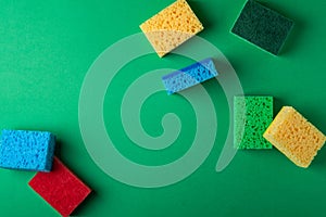 Scattered yellow, green, red, blue sponges on green colored paper background, copy space, top view, flat lay