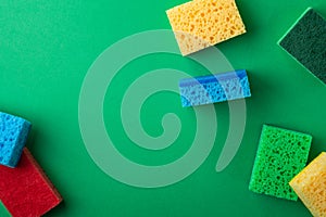 Scattered yellow, green, red, blue sponges on green colored paper background, copy space, top view, flat lay