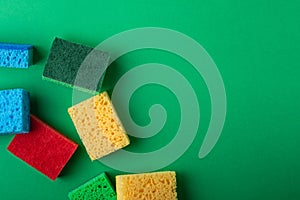 Scattered yellow, green, red, blue sponges on green colored paper background, copy space, top view, flat lay