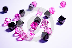 A scattering of beads on a white background, a sheet. Crystals. Iridescent and shiny pink and black beads. Materials for needlewor