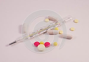 A scattering of pills on the table and a thermometer