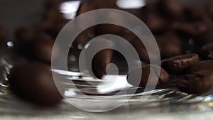 Scattering of roasted Arabica coffee beans on a glass saucer in slow motion with rotation.