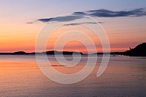 Scattering of sailboats anchored in Frenchman Bay during a pink and orange sunrise, with the Porcupine islands in silhouette