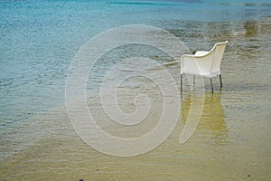 Scene of empty chair in white rattan sitting on sand beach full of clear and blue sea water background