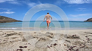 Scene on an idyllic beach of a young athlete walking on the sand and entering the water.