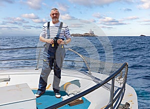 The captain of a ship stands at the bow with binoculars and looks into the camera photo