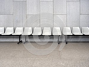 Scene of row of empty waiting chair set with white plastic seats with black iron legs seats on grey tiles.