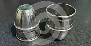 Two silver metal cups with decorative engraved patterns on a gray surface, symbolizing craftsmanship, tradition, and