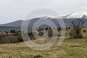 Scene with springtime mountain glade, forest, snow and residential district of bulgarian village Plana