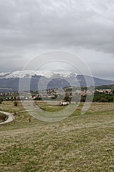 Scene with springtime mountain glade, forest, snow and residential district of bulgarian village Plana