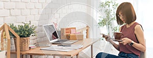 Scene of woman hold coffee cup prepare to work at desk with laptop and small parcel box use smartphone, home office dimension