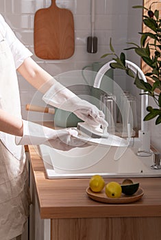 Scene with a woman washing dishes in the kitchen wearing white rubber gloves, clean background, using a brush to wash dishes