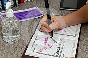 Scene of woman writes the date of her wedding in a personal organizer. canceled by coronavirus. She is sitting at a desk. A laptop