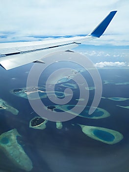 Scenery from airplane 's window. A wing of airplane, white clouds, blue sky and Maldives islands.