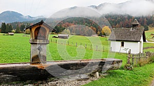 Scenery of a Bavarian farmland with a wooden trough, country houses & barns in a ranch on a foggy autumn morning