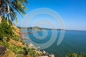 The scenery is beautiful rocky coast with palm tree, blue sea and cloudless sky in Om beach, Karnataka, India
