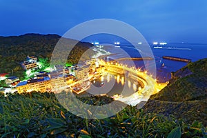 Scenery of coastal highway crossing the harbor of a fishing village with lights of fishing boats on the sea