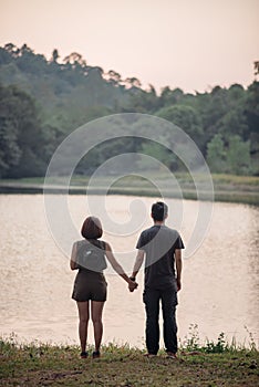 The scenery of a couple holding hands together at the lake at sunset time